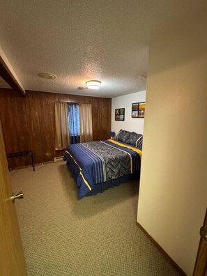 A bedroom with a bed, a window with curtains, a ceiling light, and a wall with framed pictures. - The Moose Suite Number 5 (Crosby)