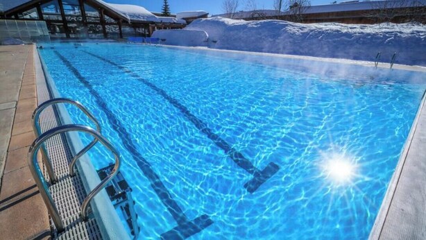 A clear blue pool with a wooden deck and a glass balustrade.
