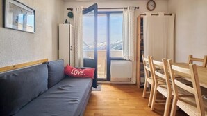 A living room with a sofa, a red pillow, a dining table with chairs, and a view through an open door.
