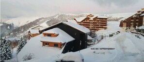 A snow-covered mountain resort with chalet-style buildings, including a prominent wooden structure with a sloped roof and a smaller building with a flat roof. - Vrbo Property (Huez)