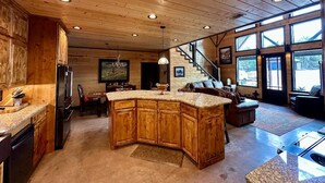 Una cocina amplia con una isla grande, armarios de madera y un comedor con una escalera que lleva a un altillo.