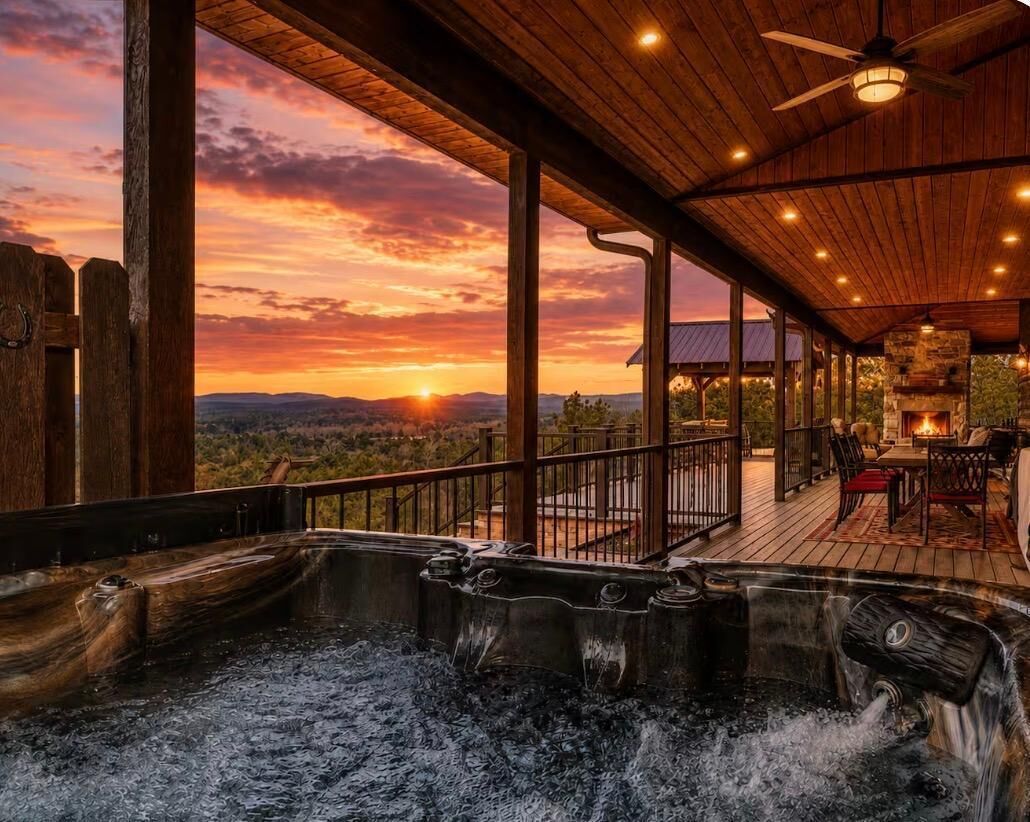 A hot tub area with a wooden deck, a fire pit, and a view of the sunset.