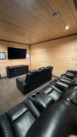 Ein Zimmer mit Holzwänden, einem an der Wand befestigten Flachbildfernseher, einer schwarzen Ledersofa und einem kleinen Schrank mit einem Fernseher.