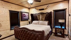 Un dormitorio con una cama grande, paredes de madera, ventilador de techo y televisor montado.