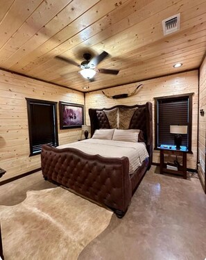 A bedroom with a large bed, wooden walls, a ceiling fan, and a mounted television. - Mack Mountain Lodge (Kirby)
