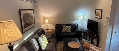 Una sala de estar con sofá, mesa de centro, lámpara y televisor.