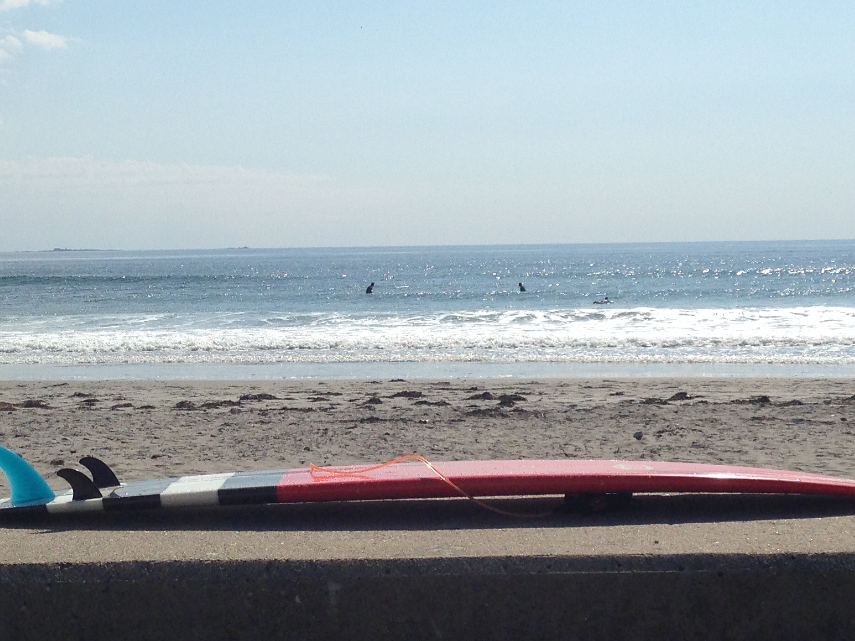 Una playa con olas, una tabla de surf y una costa lejana.