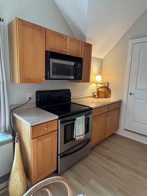 Une cuisine de taille réduite, dotée de meubles en bois, d’un four à micro-ondes, d’un four traditionnel et d’un petit plan de travail.