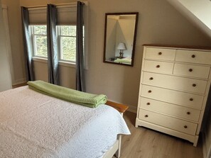 Une chambre à coucher avec un lit, une commode, un miroir et une fenêtre avec des rideaux.