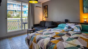 Habitación de hotel con cama, sofá, una mesita, lámpara, un cuadro y vista al balcón exterior.
