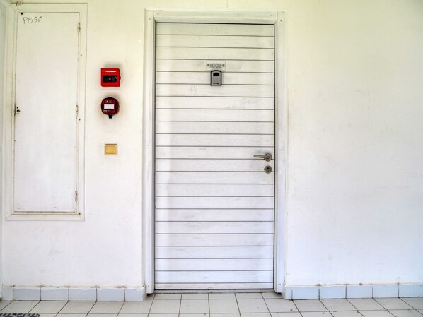 Una puerta blanca con cerradura, un buzón y un detector de incendios en la pared.