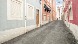 Una calle estrecha flanqueada por edificios, un cartel azul de estacionamiento y un grupo de personas a lo lejos.