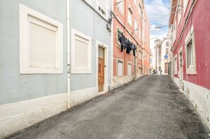 A narrow street with buildings on either side, a blue parking sign, and a group of people in the distance. - GuestReady - Modern Duplex in Lisbon (Lisbon)