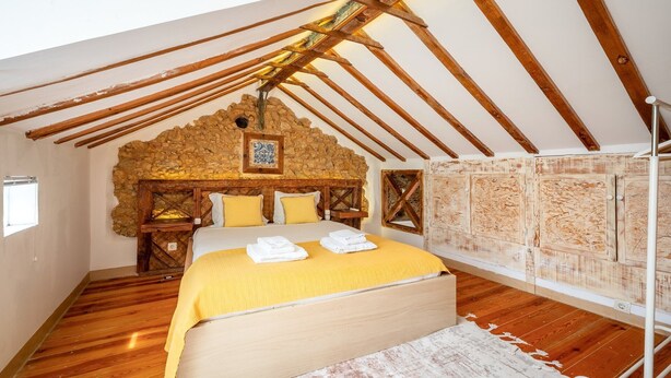 Un dormitorio con techo de madera, pared de piedra y cama con ropa de cama amarilla.