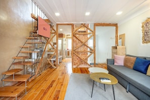 A modern interior with a wooden staircase, a stone wall, a sofa, and a coffee table. - GuestReady - Modern Duplex in Lisbon (Lisbon)