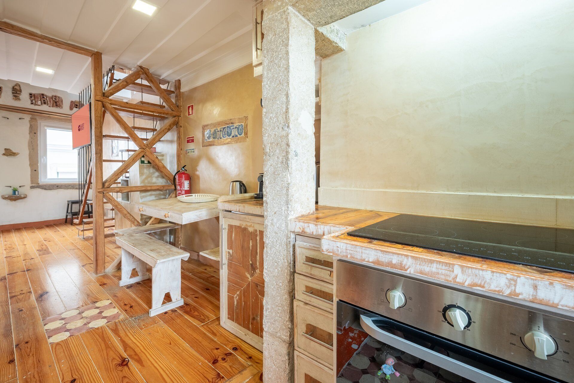 A kitchen with wooden flooring, a built-in stove, and a wooden staircase.