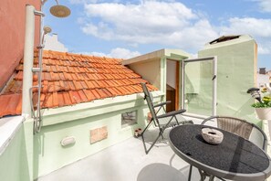 Una terrazza sul tetto con tetto in tegole, un tavolo con sedie, una pianta in vaso e una porta che dà su un ambiente interno.