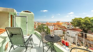 Un balcón con una silla, una mesa y vistas a la ciudad y al mar.