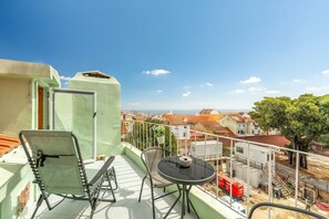 A balcony with a chair, table, and a view of the city and sea. - GuestReady - Modern Duplex in Lisbon (Lisbon)