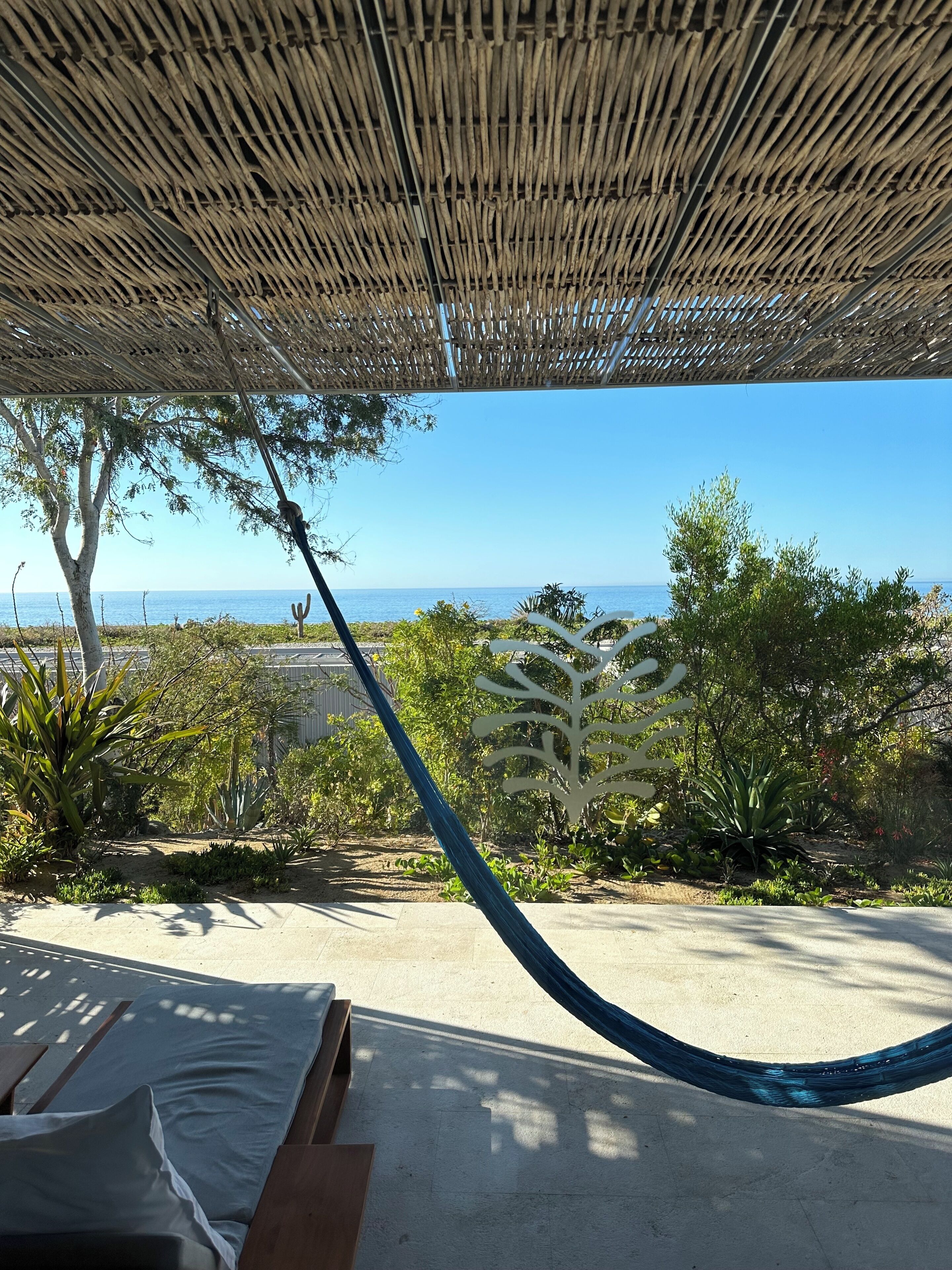 Un hamac sous un toit de chaume, un plancher en béton et une vue sur la mer.