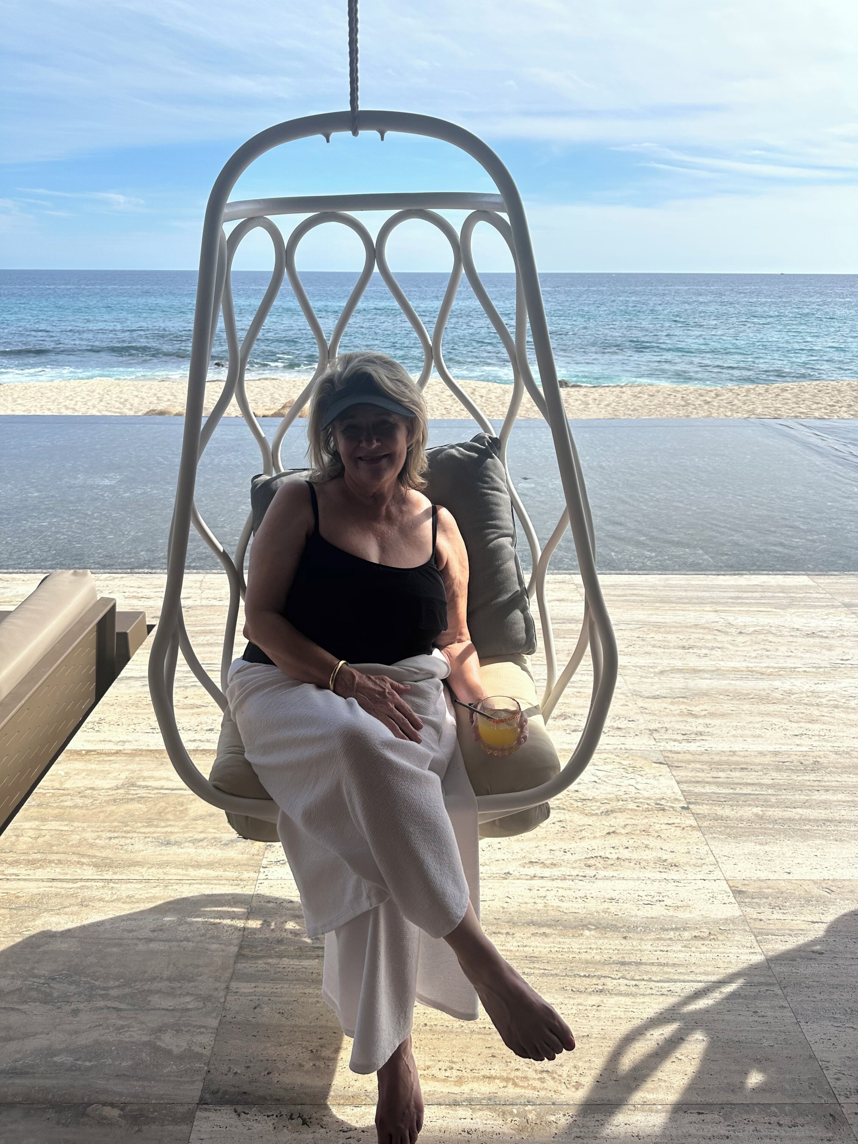 A person seated on a swing chair with a beach view.