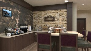 Un espace réservé au petit-déjeuner avec un mur en pierre, un panneau indiquant que le petit-déjeuner est offert gratuitement tous les jours, un coin café et une table avec des chaises.