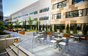 Un espace extérieur aménagé en terrasse, avec plusieurs tables et chaises, entouré de jardinières et d’arbres.