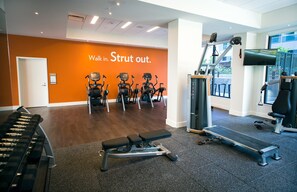 Une salle de sport équipée de tapis de course, d’un banc et d’un mur orné de messages motivants.