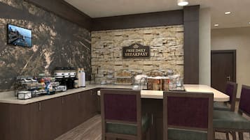 A breakfast area with a stone wall, a sign offering free daily breakfast, a coffee station, and a table with chairs.