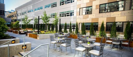 Ein Terrassenbereich im Freien mit mehreren Tischen und Stühlen, umgeben von Pflanzgefäßen und Bäumen.