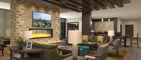 A modern hotel lobby with stone walls, a fireplace, comfortable seating, and a cityscape painting.
