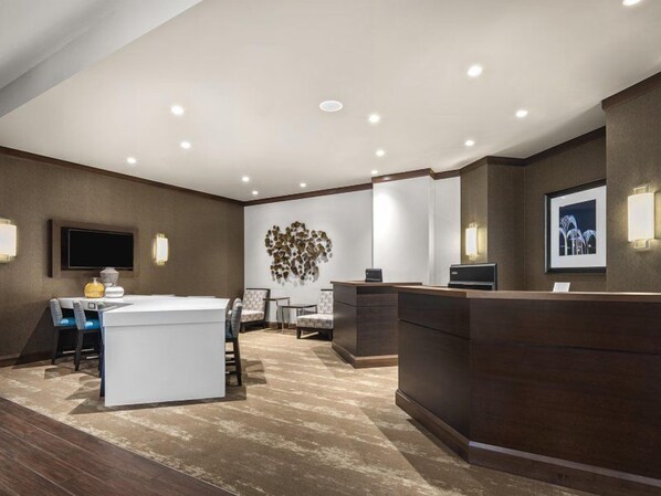 Un hall de hotel con mostrador de recepción, zona de estar y televisor de pared.