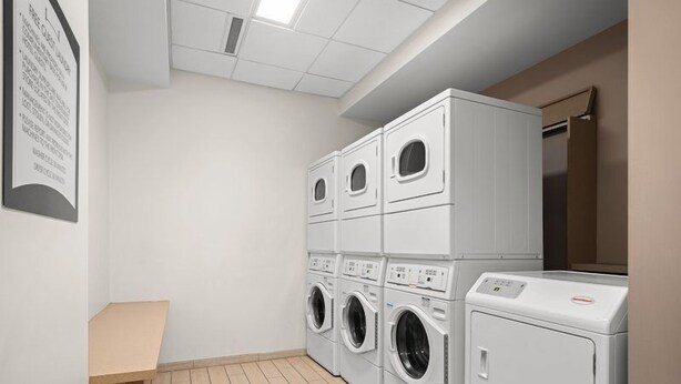 A laundry room with stacked washers and dryers, a bench, and a tiled floor.