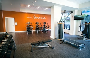 Une salle de sport équipée de tapis de course, d’un banc et d’un mur orné de messages motivants.