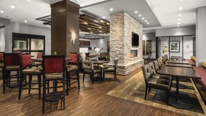 A modern hotel lobby with a stone fireplace, wooden flooring, and a mix of seating arrangements including tables and chairs.