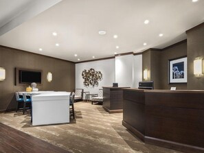 Un hall de hotel con mostrador de recepción, zona de estar y televisor de pared.