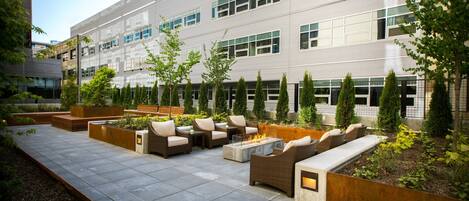 An outdoor seating area with fire pits, planters, and a modern building in the background.