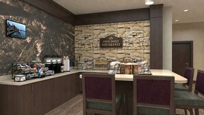Un espace réservé au petit-déjeuner avec un mur en pierre, un panneau indiquant que le petit-déjeuner est offert gratuitement tous les jours, un coin café et une table avec des chaises.