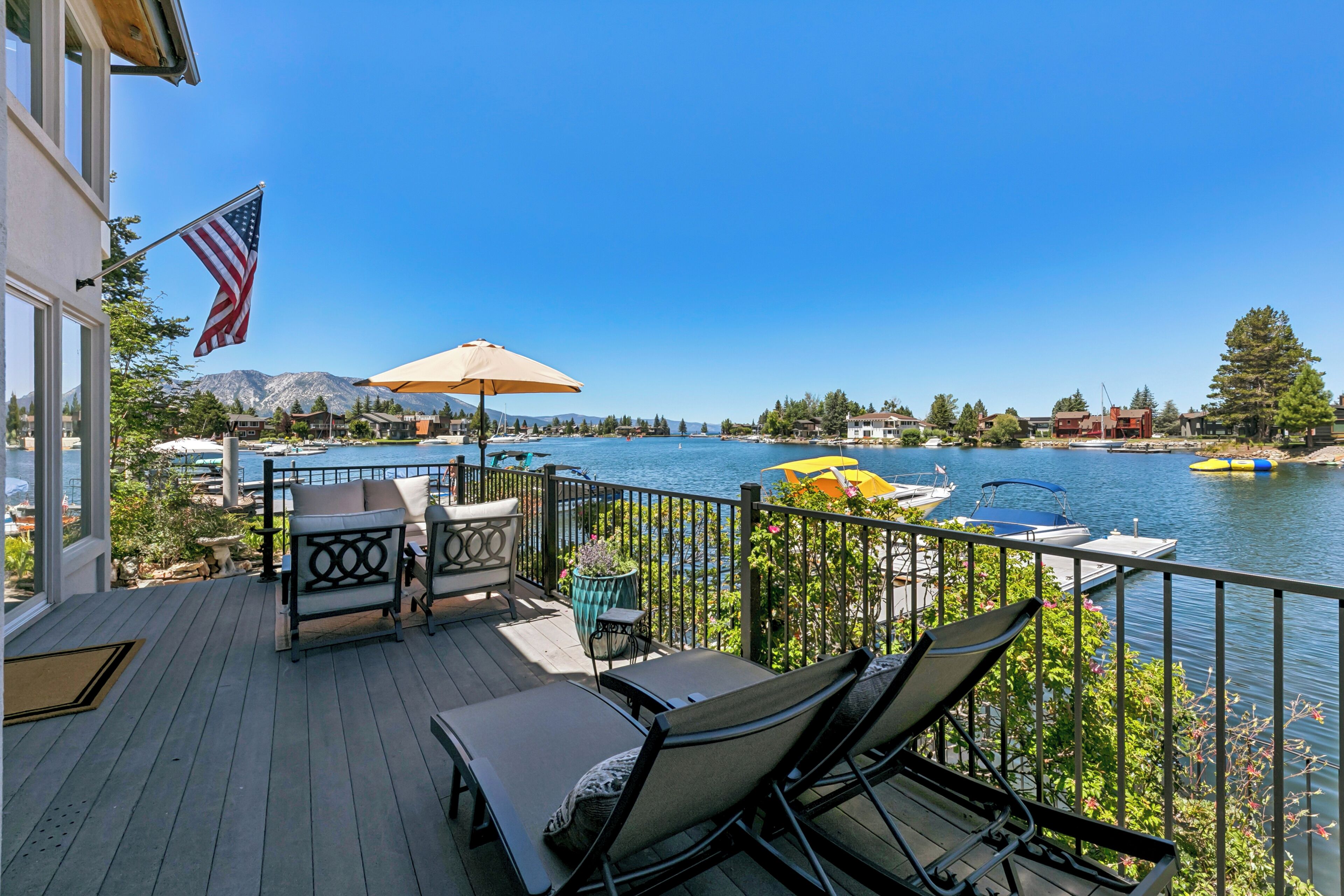 A deck with outdoor furniture, a flag, and a view of a lake with boats.
