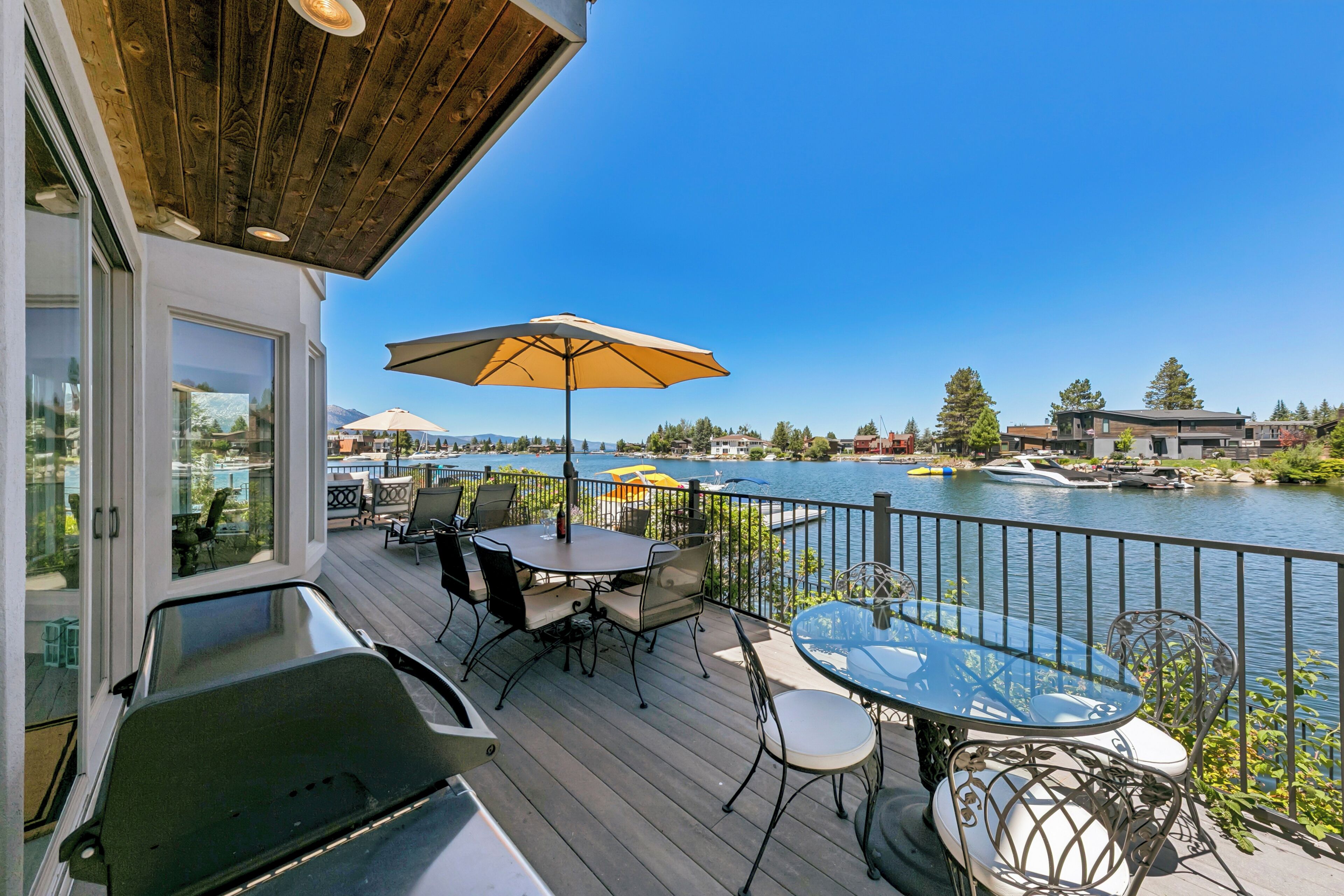 A deck with outdoor furniture, a table, and an umbrella overlooking a body of water.