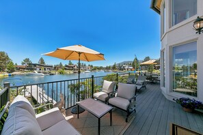 Terraza con mobiliario exterior, un sombrilla grande y vista a un lago con barcos.