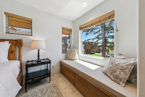 A bedroom with a bed, bedside table, lamp, window seat with cushions, and a view of the outdoors. - Tahoe Keys Easy Lake Access w/ Boat Dock, BBQ (South Lake Tahoe)