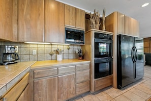 Eine moderne Küche mit Holzschränken, integriertem Mikrowellenherd, einem Edelstahlkühlschrank und einer Kaffeemaschine.