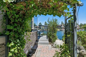 Un sendero de piedra conduce a una entrada con puerta, con vista a un lago y casas al fondo.