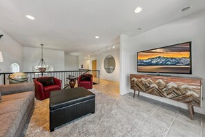 Ein modernes Wohnzimmer mit einem Flachbildfernseher, roten Ledersofas, einem schwarzen Hocker und einem dekorativen Schrank.