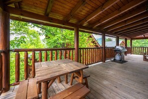 Eine Holzterrasse mit Picknicktisch und Grill, umgeben von einem Holgitter und üppigem Grün.