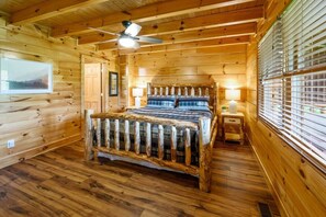 Ein Schlafzimmer einer Holzhütte mit einem Bett, einem Deckenventilator und einem Fenster mit Jalousien.