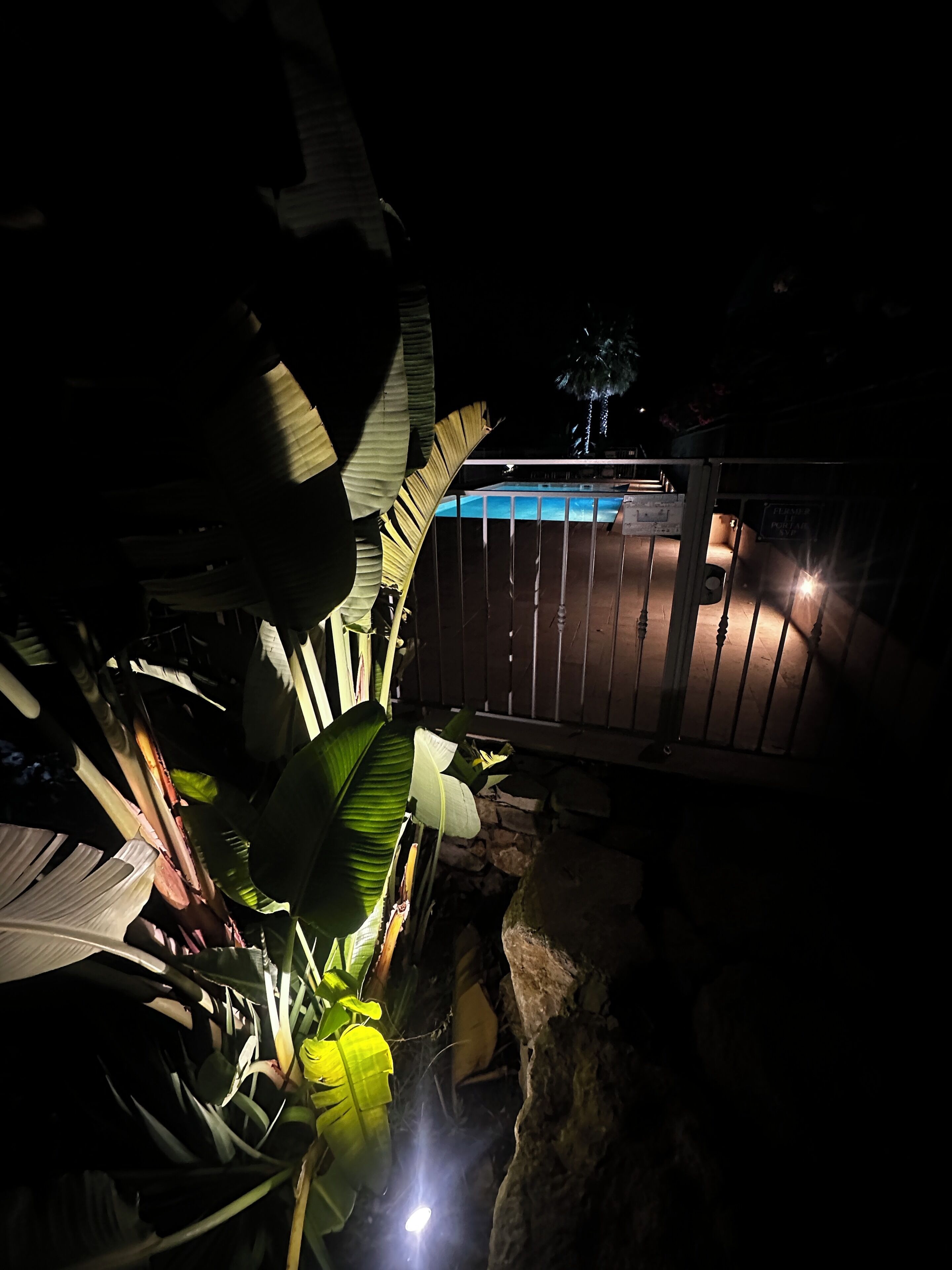 Vista nocturna de una zona de piscina con terraza de madera y pared de piedra.