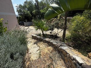 A garden pathway with a stone wall, various plants, and a parked car. - Spacious 150-square-meter penthouse with a 180-degree panoramic ocean view. (Roquebrune-sur-Argens)