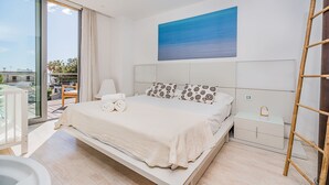 Een moderne slaapkamer met een groot bed, uitzicht op zee door het raam, en een balkon met een stoel.